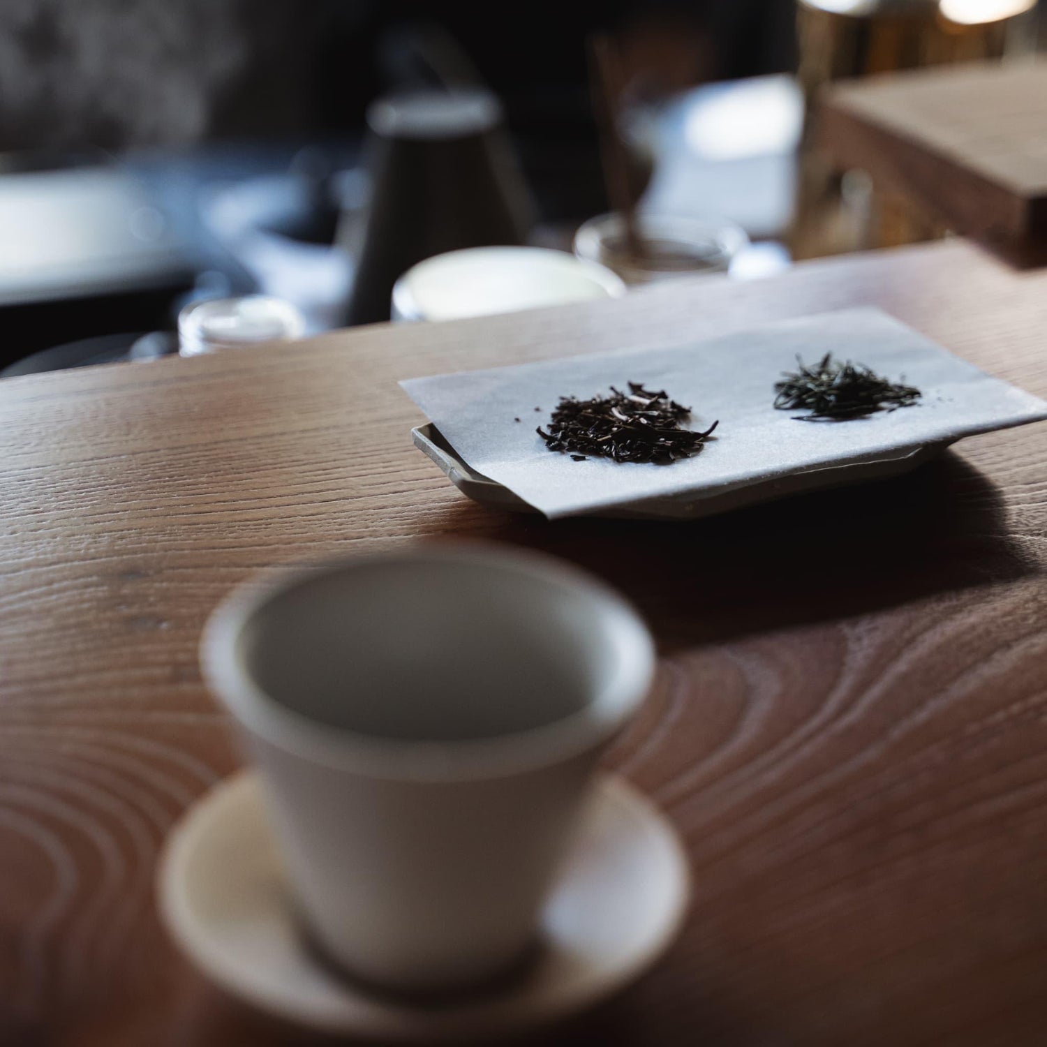 Beautiful white tea bowl and loose tea leaves on a traditional Japanese wooden table.