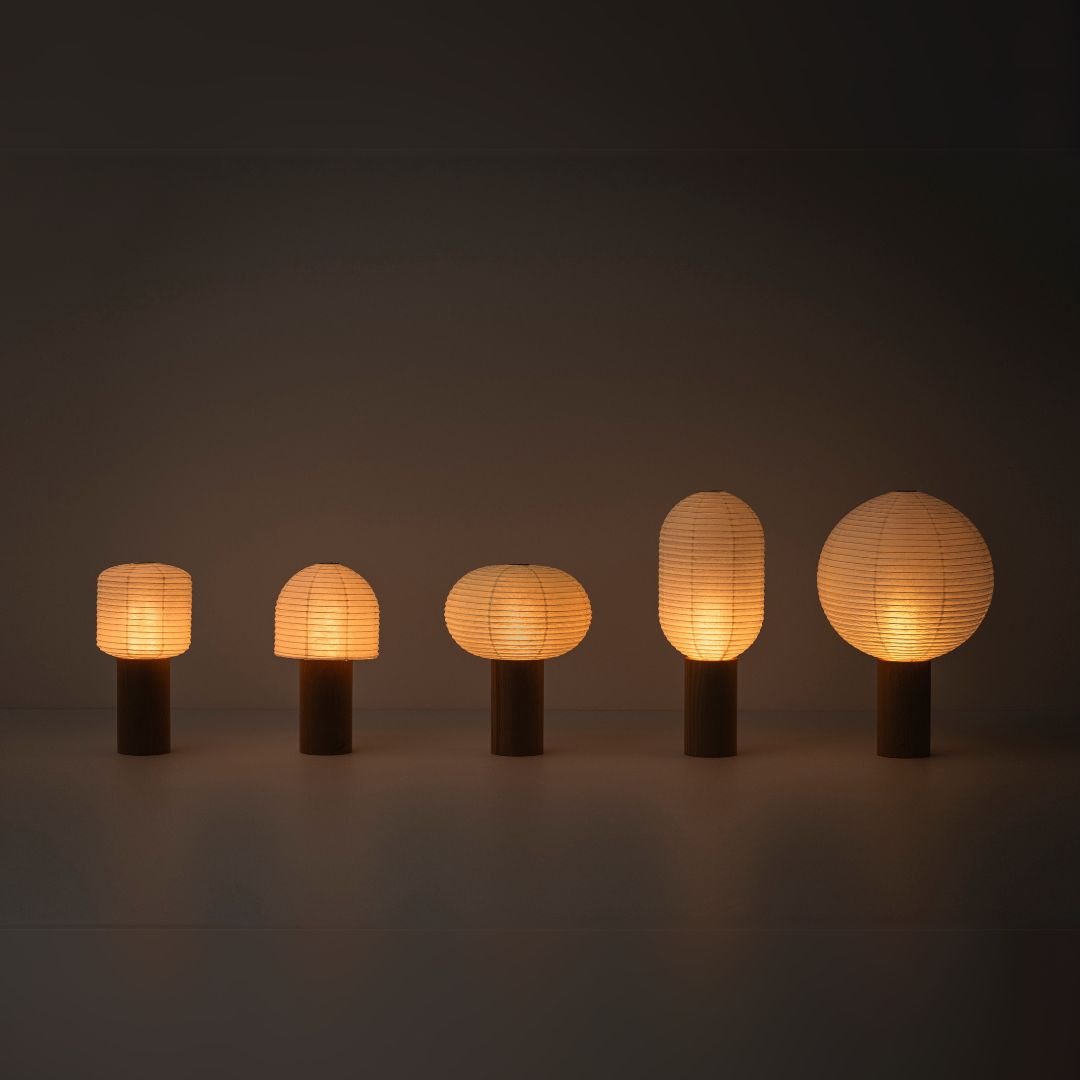 Fünf tragbare Papierlampen, „TORCHIN“, mit warmem Licht, aufgereiht in einem schwach beleuchteten Raum. Die Lampenschirme bestehen aus japanischem Washi-Papier von Yame-Chochin-Laternen, und jede Lampe hat einen hölzernen zylindrischen Griff.