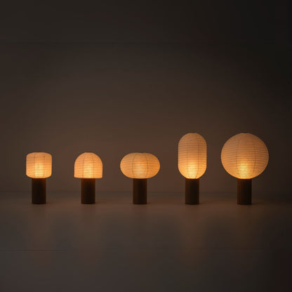 Fünf tragbare Papierlampen, „TORCHIN“, mit warmem Licht, aufgereiht in einem schwach beleuchteten Raum. Die Lampenschirme bestehen aus japanischem Washi-Papier von Yame-Chochin-Laternen, und jede Lampe hat einen hölzernen zylindrischen Griff.