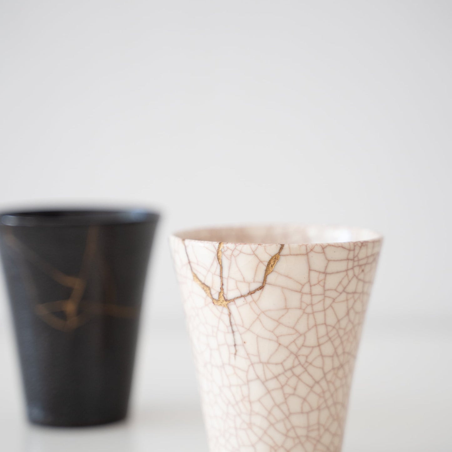 Hvide og sorte keramikkrus repareret med kintsugi, en traditionel japansk kunstform til at reparere knust keramik med guldlak, der viser skønheden i ufuldkommenhed og omfavner konceptet wabi-sabi.