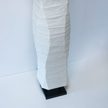 Vue en gros plan, sous un angle, de la partie inférieure d'une lampe en papier japonais washi, montrant son design épuré sur fond blanc