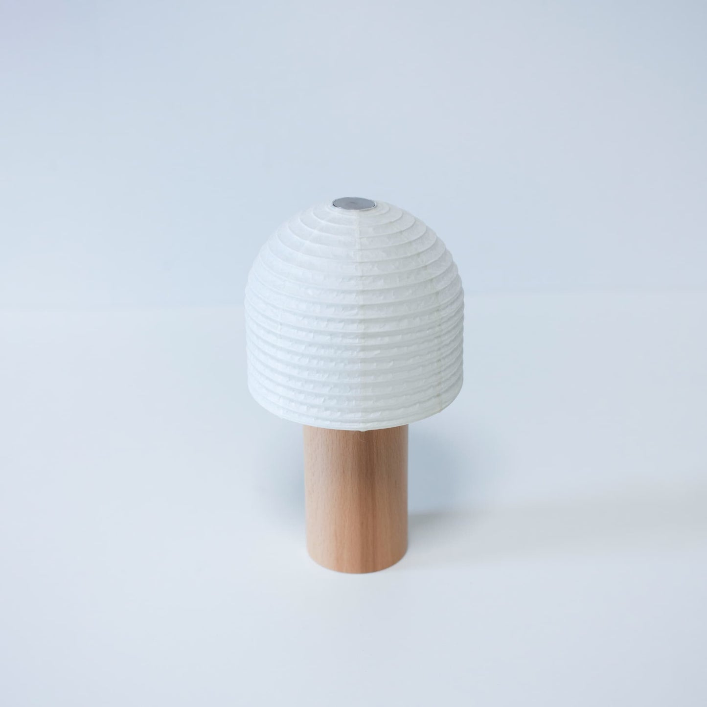 A Japanese paper lantern with a bell-shaped paper top and wooden handle against a bright white background