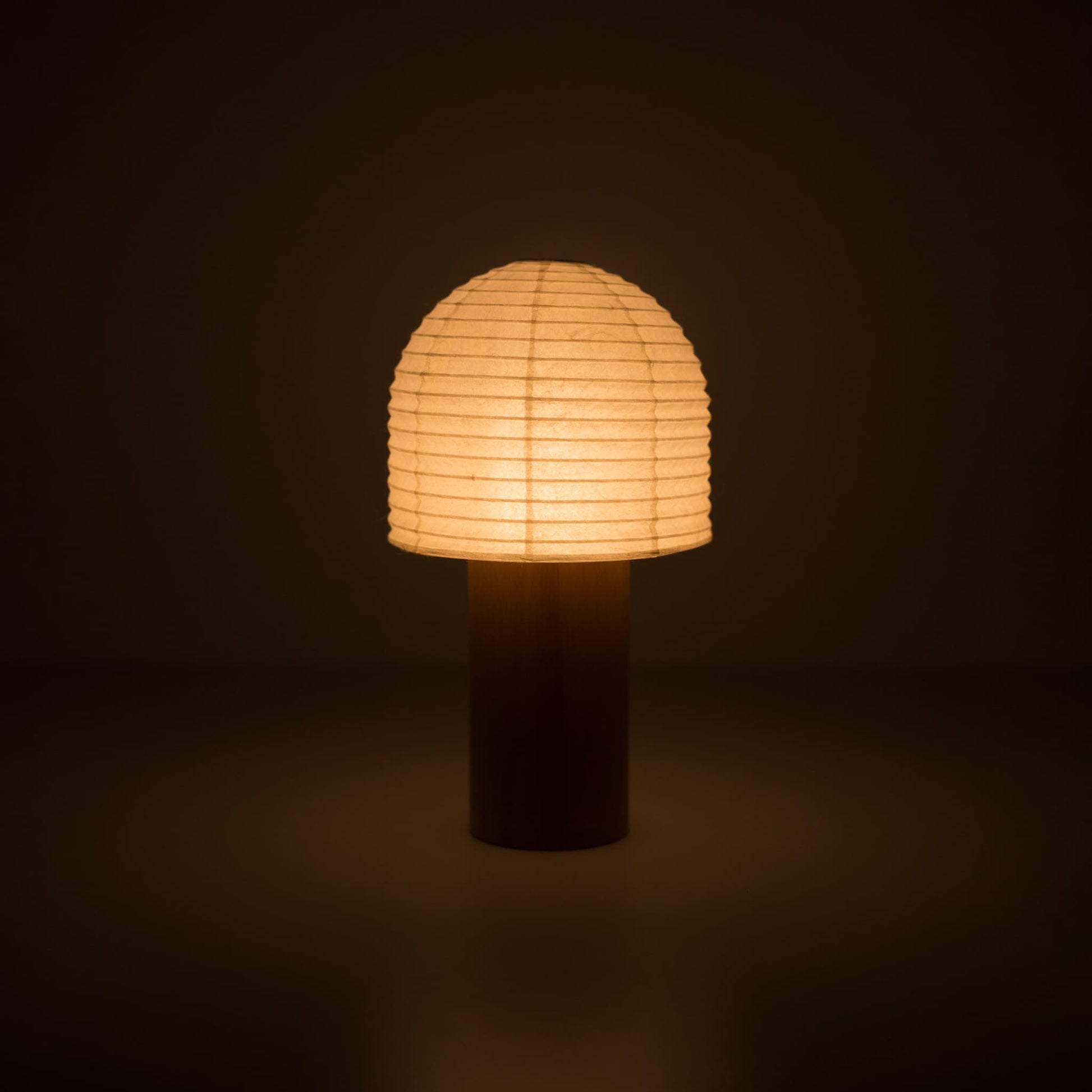 A portable Japanese paper lantern with a wooden handle and bell-shaped top, glowing warmly in a dark room