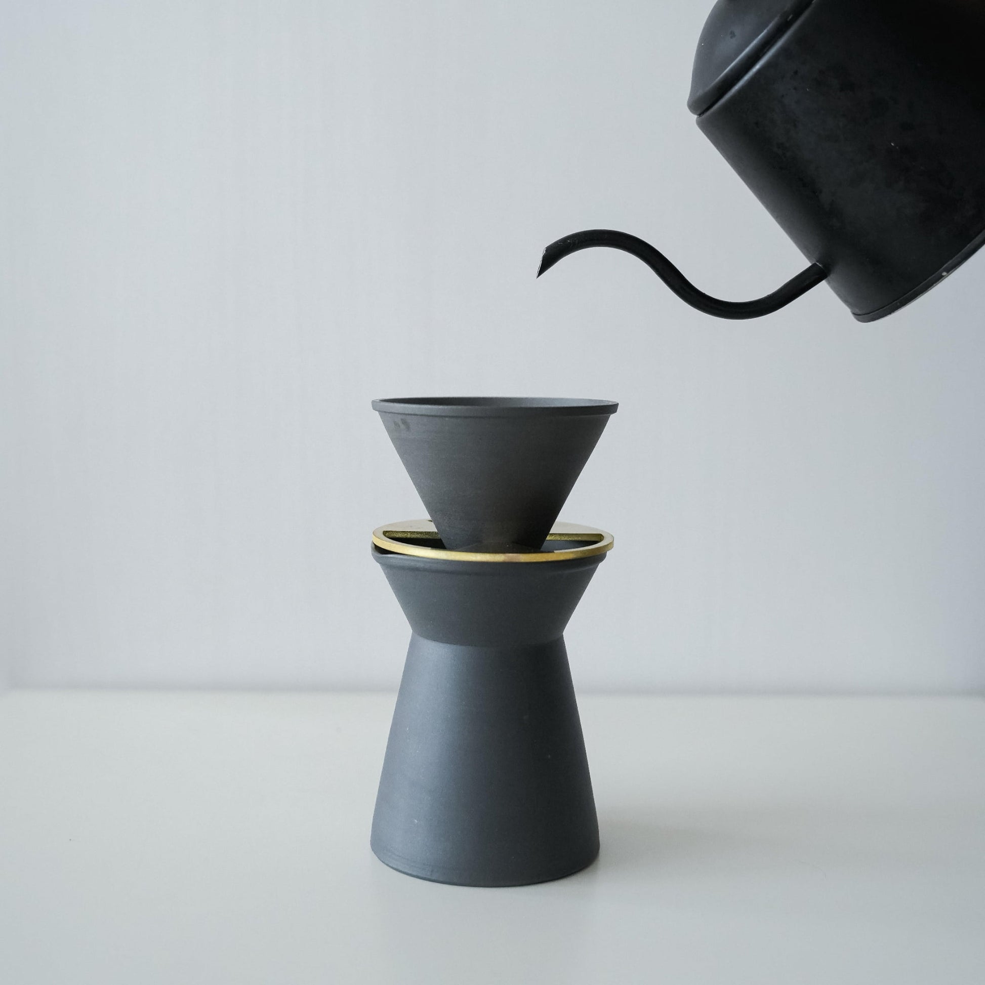 Hældning af varmt vand fra en sort gryde i et minimalistisk sort Banko ware kaffeserver og drypsæt.