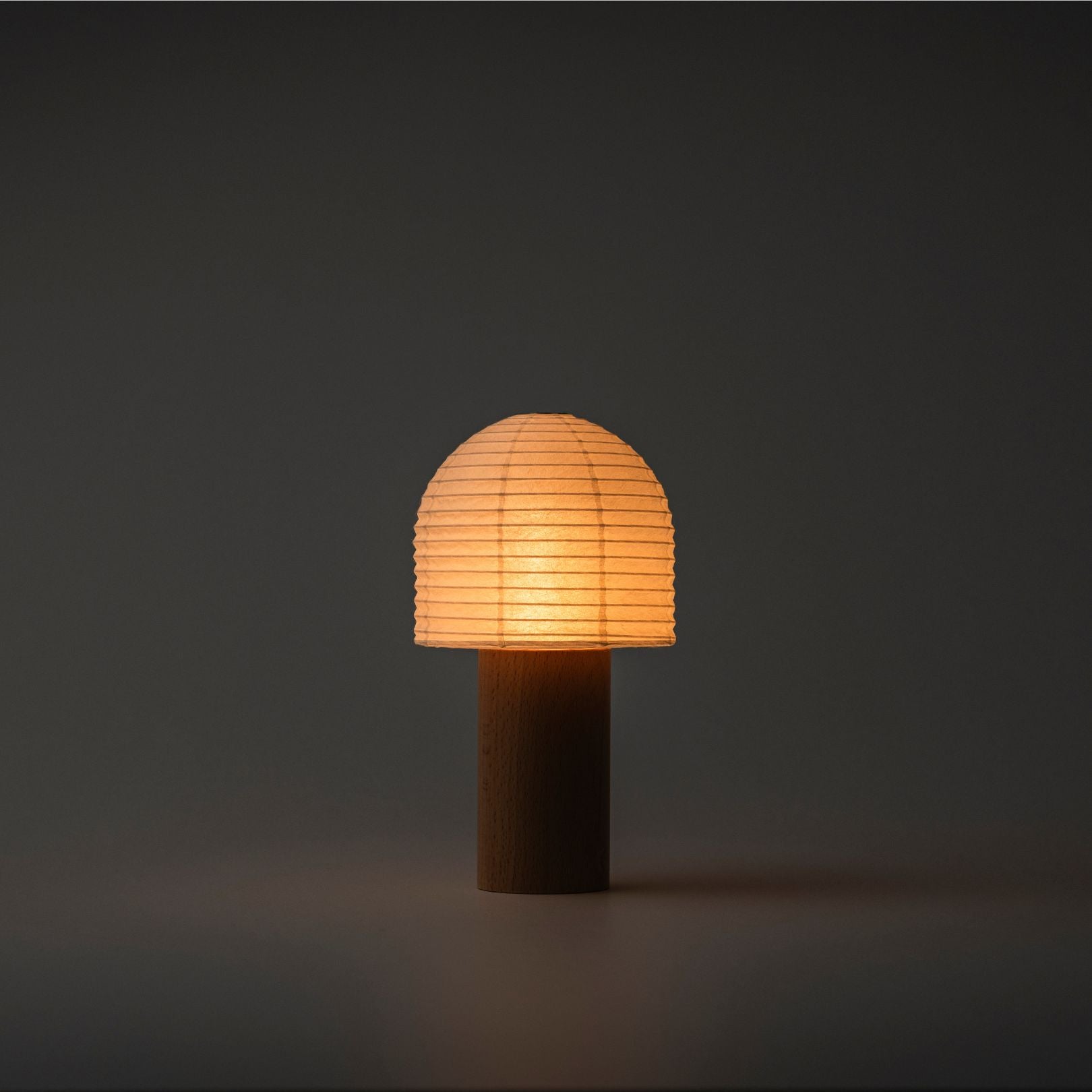 A brightly glowing Japanese paper lantern with a bell-shaped paper top and wooden handle in a dark room