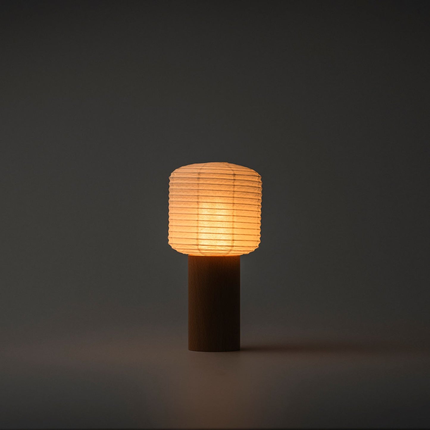 Eine tragbare Papier-Tischlampe, die in einem dunklen Raum helles warmes Licht ausstrahlt, mit einem Holzgriff und einer Papierhaube