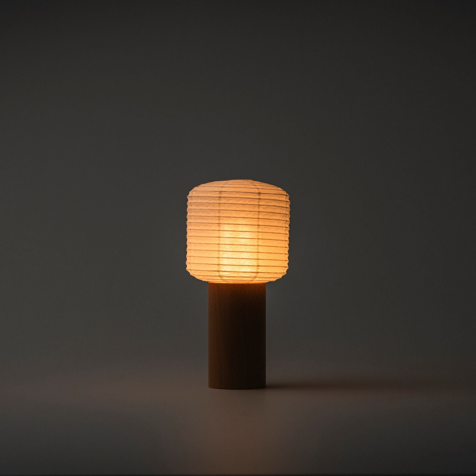 Eine tragbare Papier-Tischlampe, die in einem dunklen Raum helles warmes Licht ausstrahlt, mit einem Holzgriff und einer Papierhaube