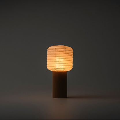 Eine tragbare Papier-Tischlampe, die in einem dunklen Raum helles warmes Licht ausstrahlt, mit einem Holzgriff und einer Papierhaube