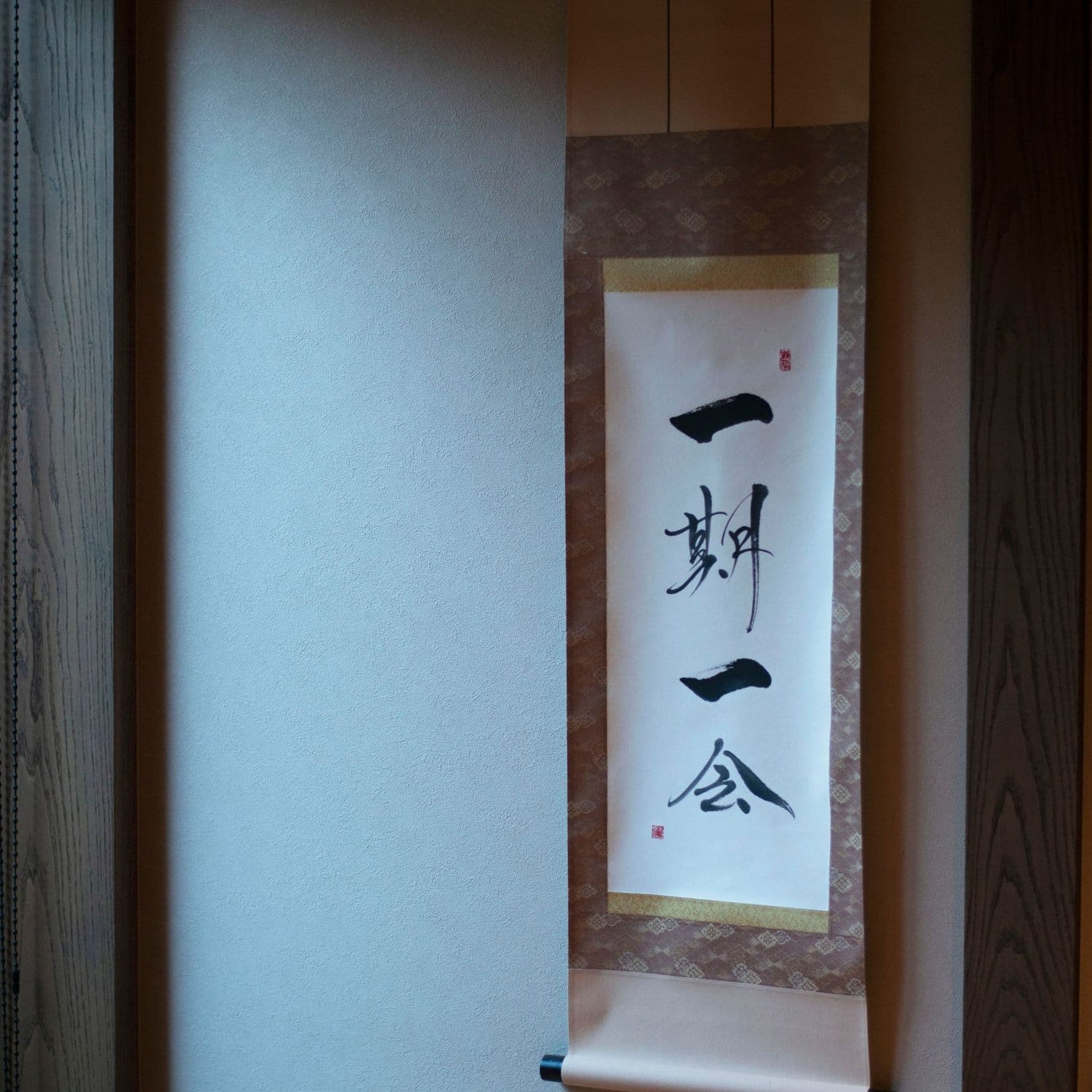 Seitenansicht einer traditionellen japanischen Hängerolle mit Kalligrafie „一期一会“ (schätze jede Begegnung), ausgestellt in einer japanischen Nische. 
