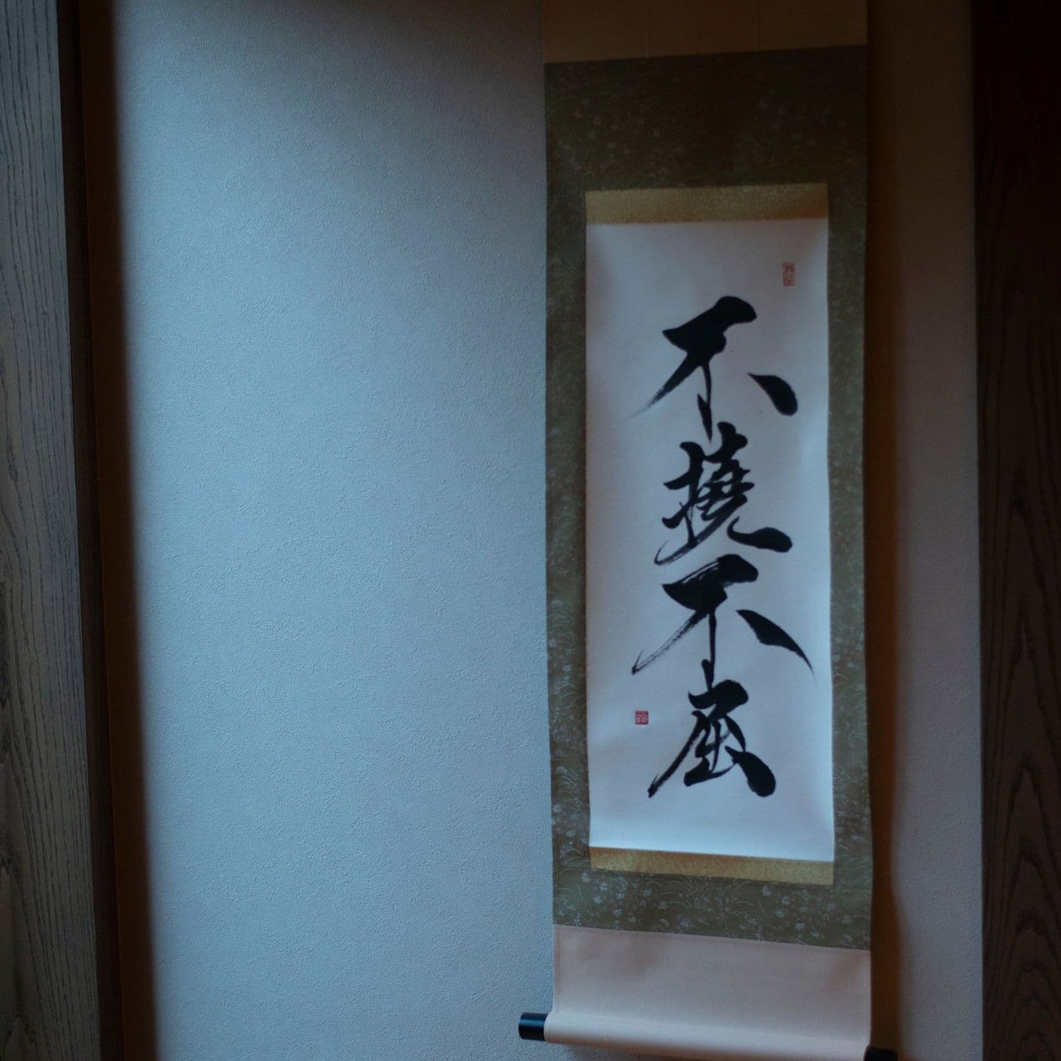Seitenansicht einer Hängeschriftrolle in einer japanischen Nische mit der Kalligrafie „不撓不屈“ (Unbeugsamer Geist)