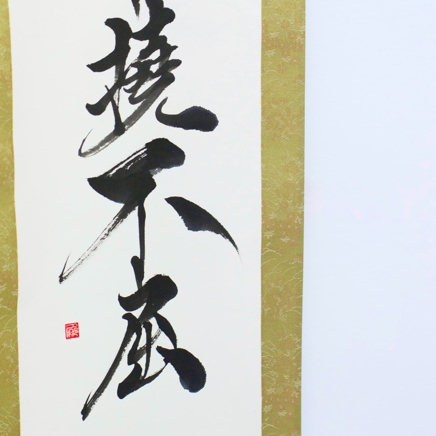 "Eine Nahaufnahme der unteren linken Ecke einer traditionellen japanischen Hängerolle, die die Kalligrafie '撓不屈' (Entschlossen und Unnachgiebig) zeigt"