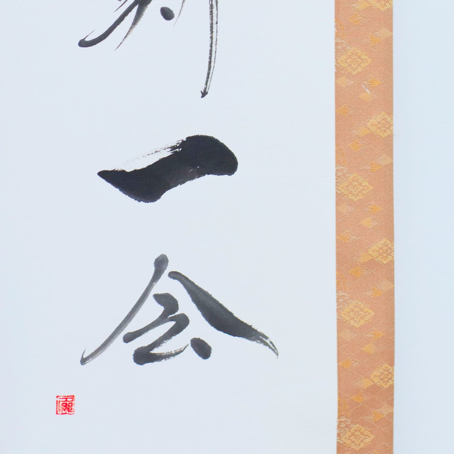 Nahaufnahme der unteren linken Ecke einer Hänge-Schriftrolle, die sich auf die japanische Kalligrafie für '一会' (eine Begegnung) konzentriert
