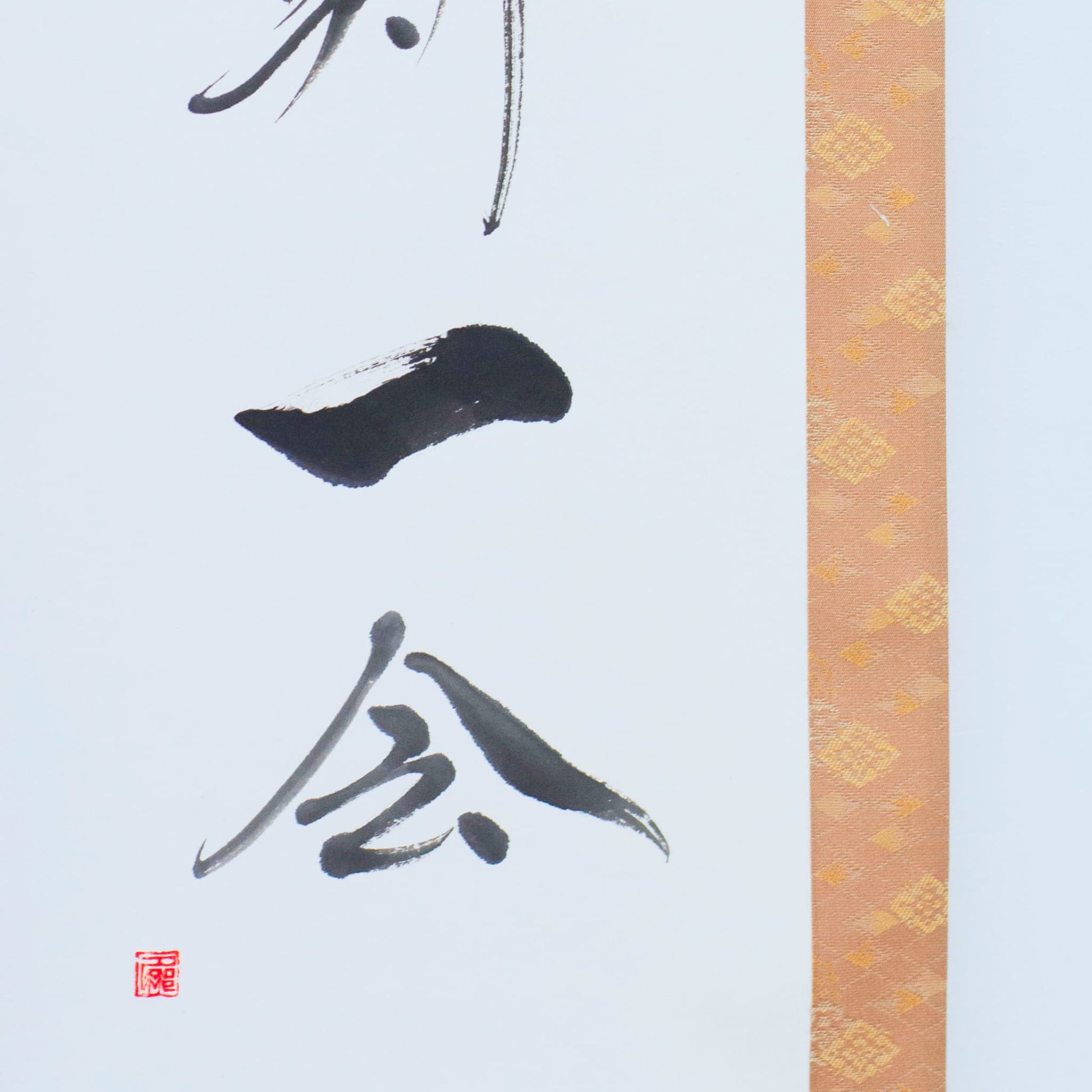 Nahaufnahme der unteren linken Ecke einer Hänge-Schriftrolle, die sich auf die japanische Kalligrafie für '一会' (eine Begegnung) konzentriert