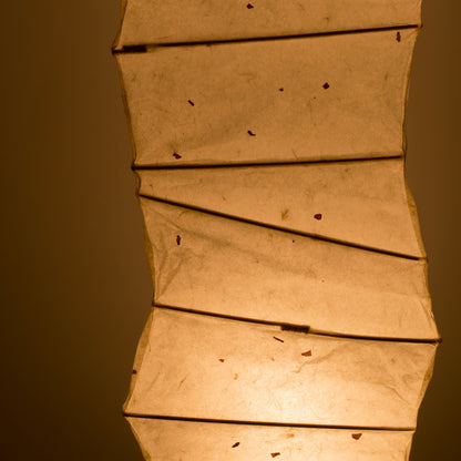 "Vue latérale détaillée d'une lampe japonaise incurvée en papier washi, mettant en valeur les motifs washi illuminés sur fond brun"