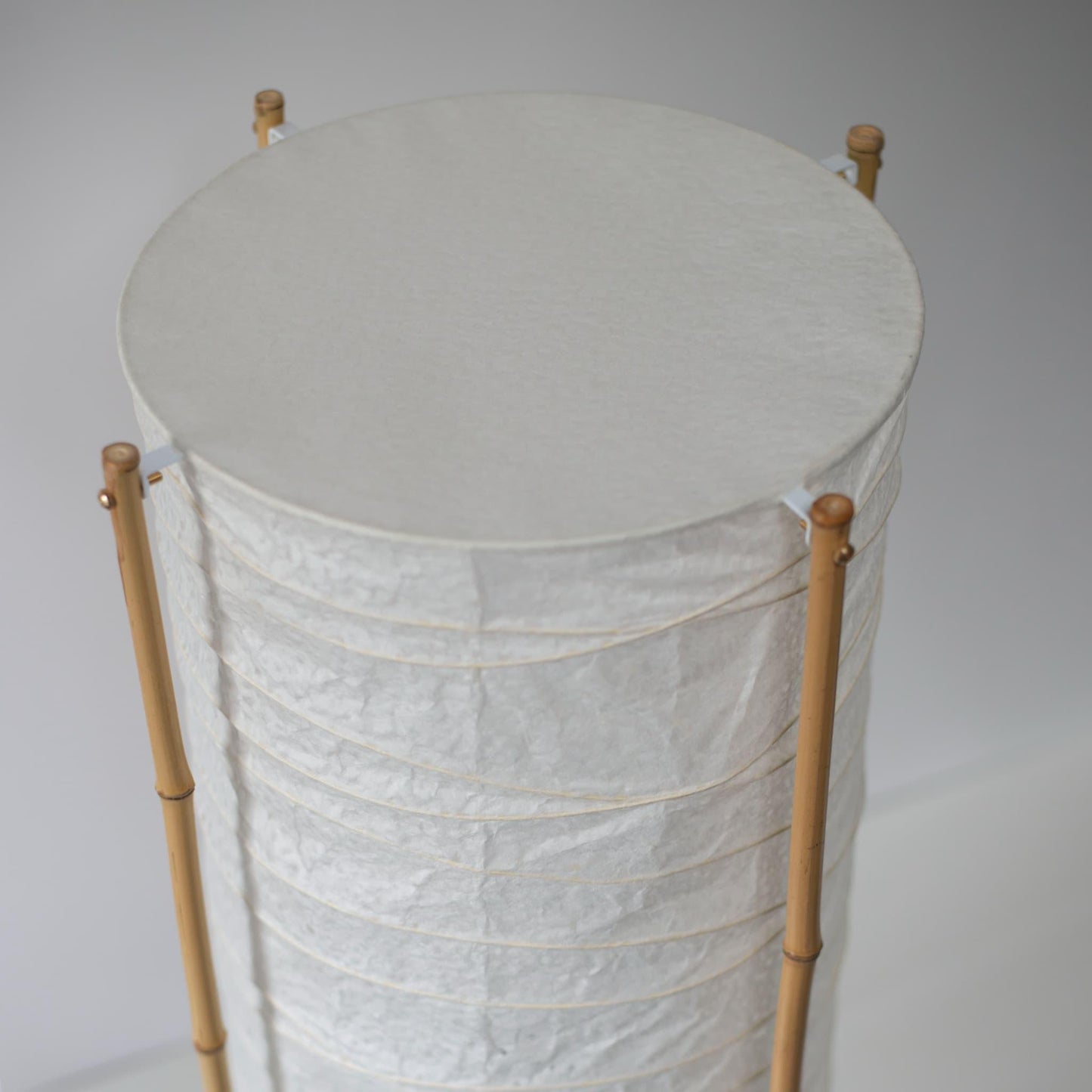 Gros plan de la partie supérieure d'une lampe japonaise cylindrique avec cadre en bambou et papier washi, fond blanc