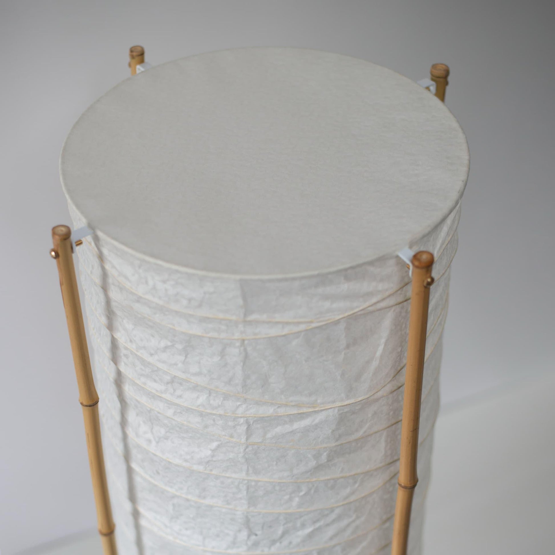 Gros plan de la partie supérieure d'une lampe japonaise cylindrique avec cadre en bambou et papier washi, fond blanc
