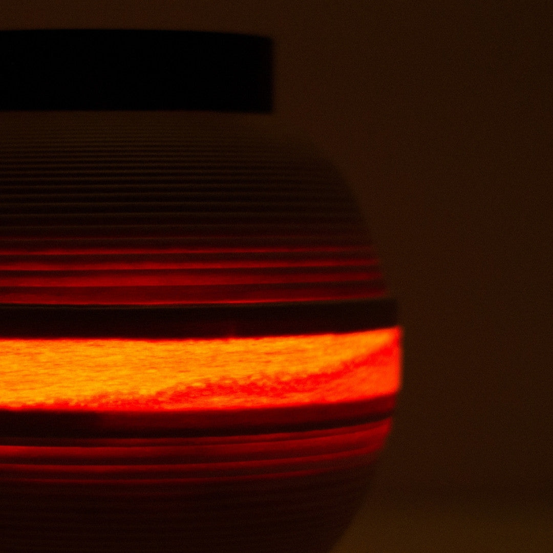 Close-up van een Japanse woonkamerlamp met een warme lichtband die door beuken houten lamellen schijnt.