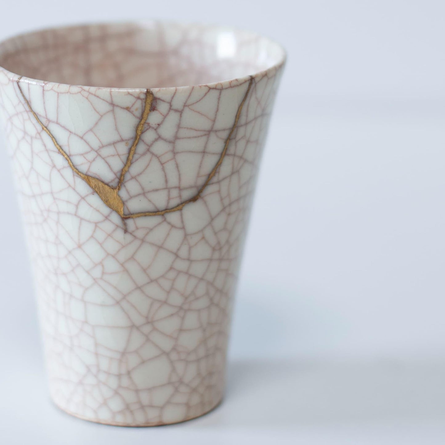 Hvid kop repareret med Kintsugi, en traditionel japansk teknik, præsenteret i en paulownia-trækasse med inskriptionen "Kintsugi".