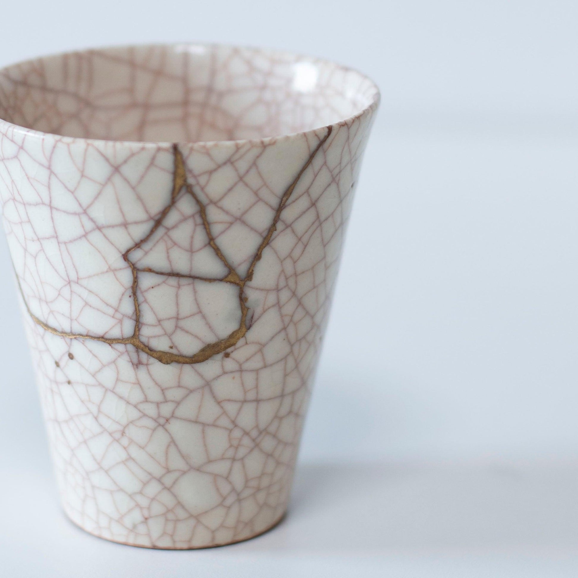 Hvid kop repareret med Kintsugi, en traditionel japansk teknik, præsenteret i en paulownia-trækasse med inskriptionen "Kintsugi".
