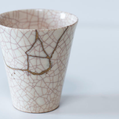 Hvid kop repareret med Kintsugi, en traditionel japansk teknik, præsenteret i en paulownia-trækasse med inskriptionen "Kintsugi".