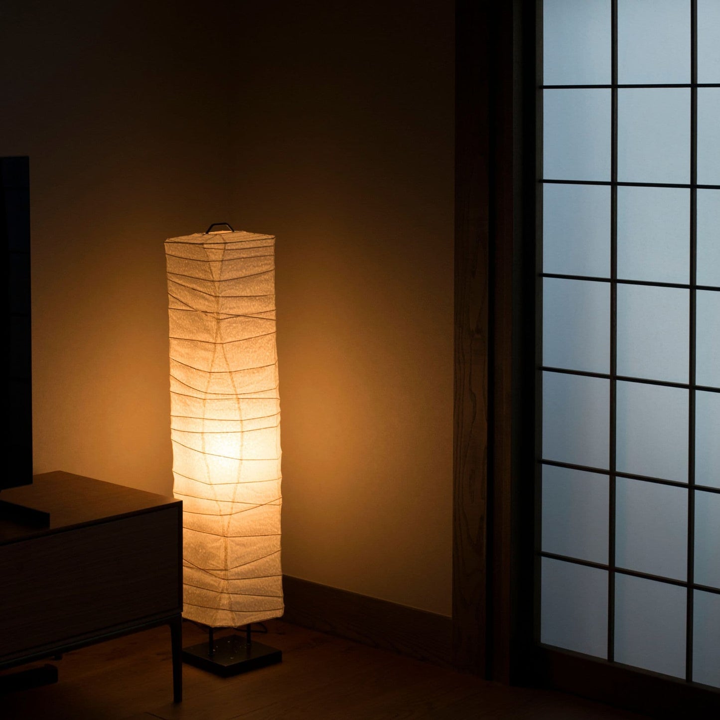 Un lampadaire japonais en papier lumineux aux lignes courbes, placé dans le coin d'une pièce japonaise traditionnelle. 