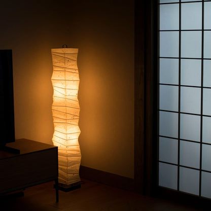 "Lampe de sol japonaise en papier avec des courbes hautes et aléatoires, placée dans le coin d'une pièce japonaise traditionnelle, émettant une lumière chaude." 