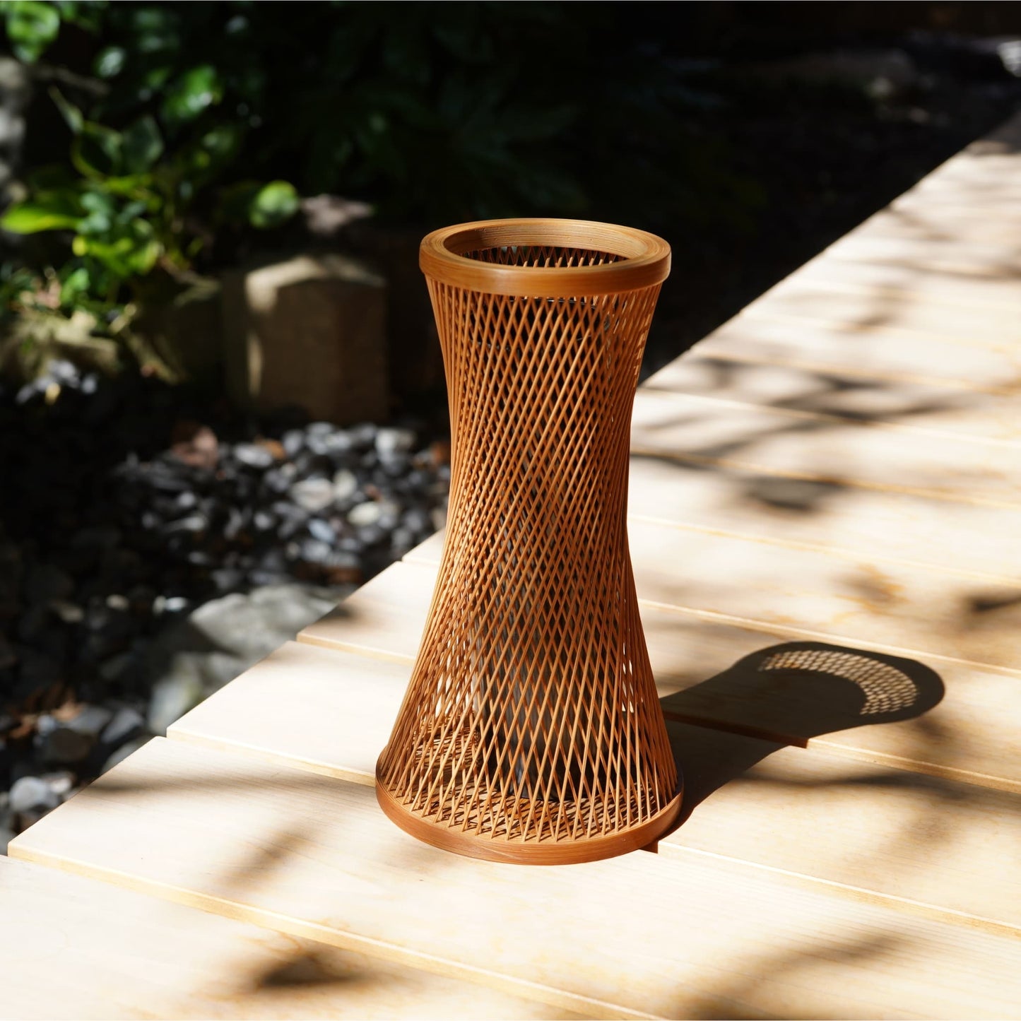 cylindrisk japansk ikebana-vase lavet af bambus med indviklede, flettede strimler, placeret på en engawa (veranda).