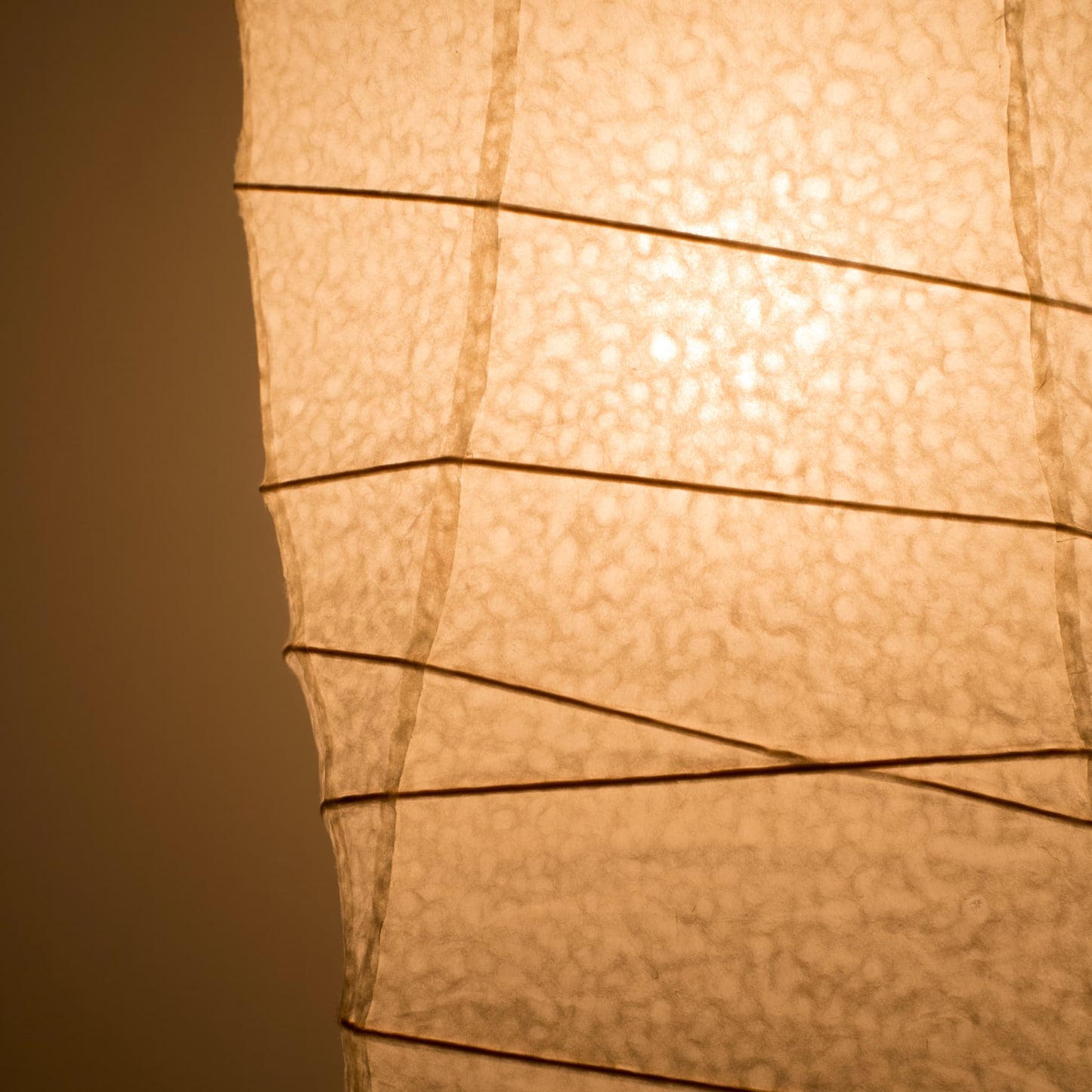 Gros plan de côté d'une lampe japonaise en papier washi, avec une lumière chaude illuminant la texture détaillée du papier washi