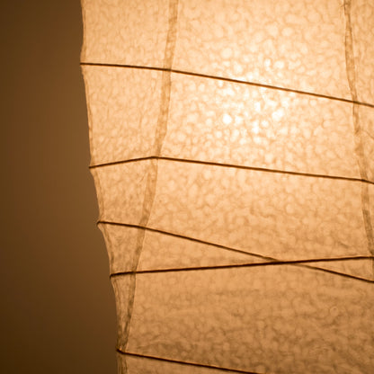 Gros plan de côté d'une lampe japonaise en papier washi, avec une lumière chaude illuminant la texture détaillée du papier washi