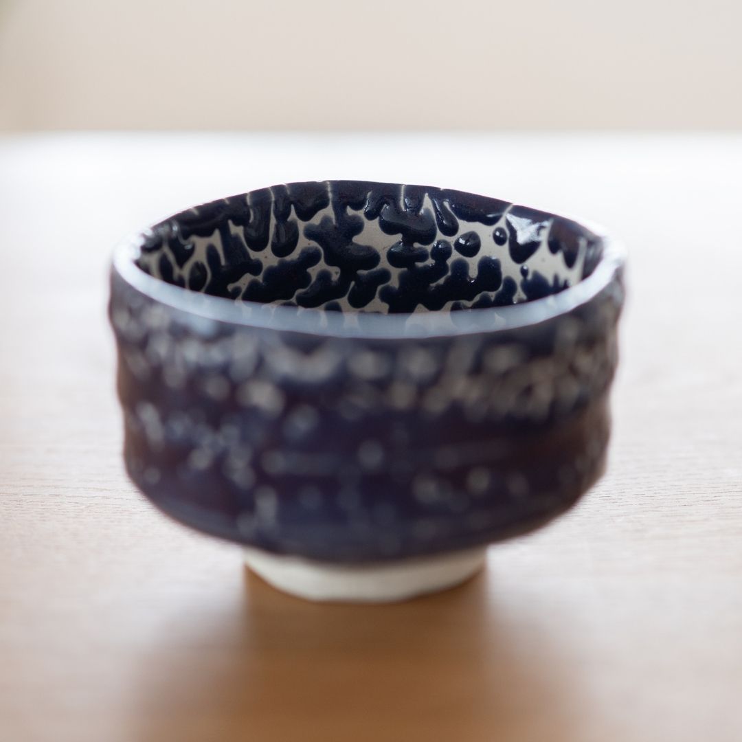 japansk Shino Ware matcha-skål "Midnight Blue Kairagi" udstillet på en træoverflade, der fremhæver skålens form, den rige mørkeblå farve og den teksturerede Kairagi-glasur.