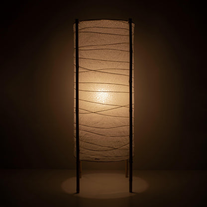 "Vue complète d'une lampe japonaise cylindrique avec abat-jour en papier washi et cadre en bambou, lumière chaude sur fond marron"