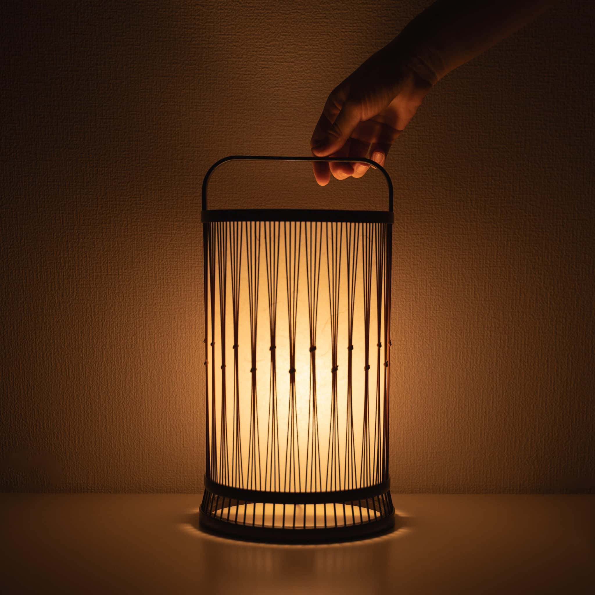 "Hand hält eine traditionelle japanische Bambuslampe, handgefertigt in Shizuoka mit 800 Jahre alten Techniken."