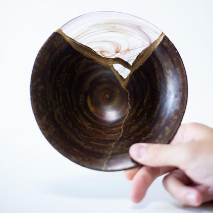 Eine Hand, die eine Kintsugi-Schale hält und das Gewicht und die Balance des Stücks zeigt.