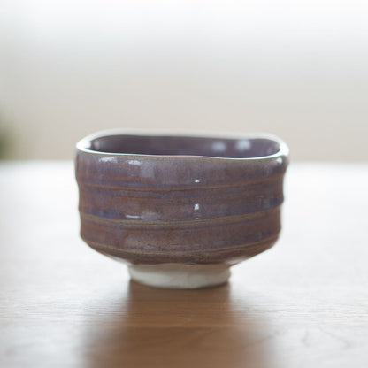 Ganzansicht einer handgefertigten, blassvioletten Matcha-Chawan-Schale mit modernen japanischen Ästhetikmerkmalen, handgeschnitzten Rillen und einem weißen Porzellanboden, die ruhige Eleganz verkörpert.