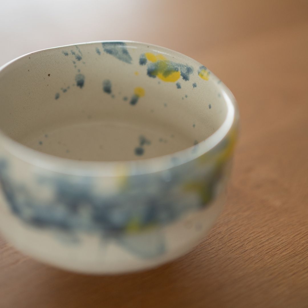 Nahaufnahme des inneren Randes der handgefertigten Matcha-Schale "Splash", die die dynamischen blau-gelben Muster hervorhebt, die durch eine spezielle Flicktechnik von Shinzan Kiln-Handwerkern entstanden sind.