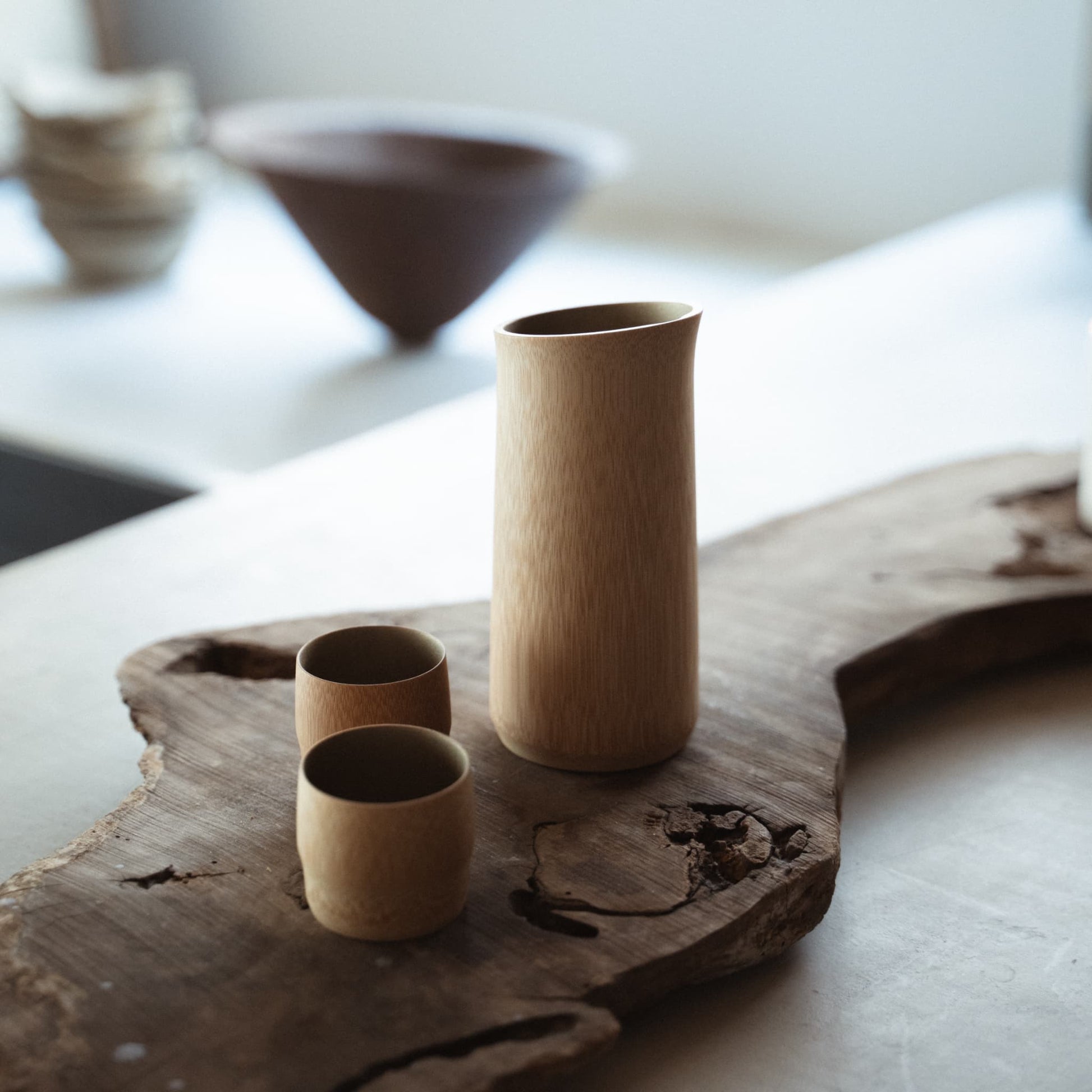 "Japandi-Tafeldekoration mit Treibholztisch, darauf ein Sake-Set aus Bambus, handgefertigt nach traditionellen Techniken aus Kyoto, Japan."