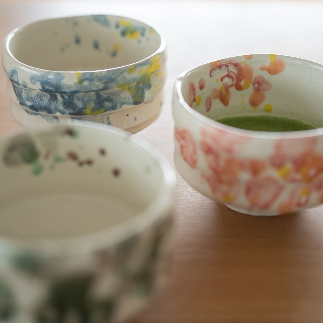 "Sammlung japanischer Matcha-Schalen (Blume, Spritzer, Wald) für die Teezeremonie, die das leuchtende Grün des Matcha im Kontrast zur rosa-weißen Glasur hervorheben."