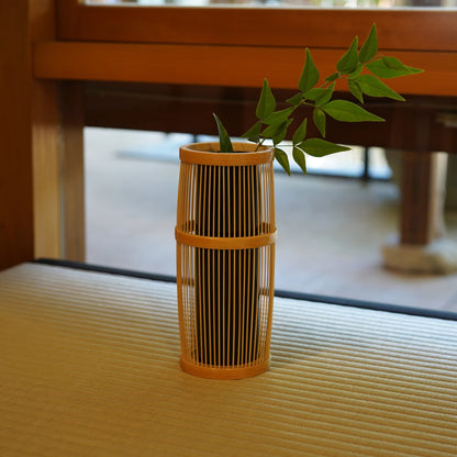 japansk ikebana-vase med grønne planter, placeret på en tatami-måtte i et traditionelt japansk rum.