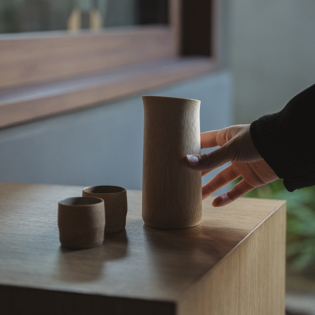 Japanisches Bambus-Sake-Set – Zinn-Makie auf einem Holztisch mit einer Hand.