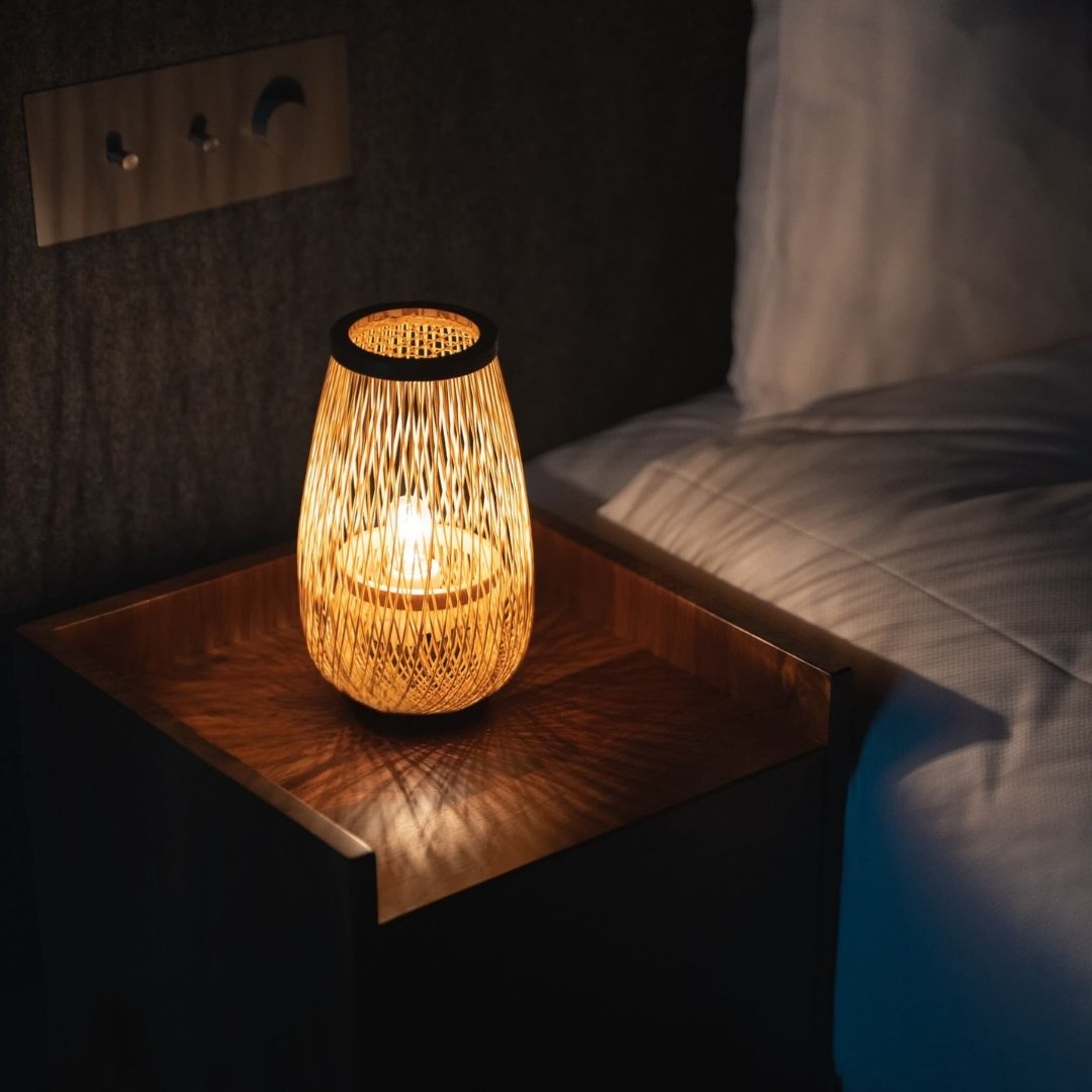 "Een Japanse bamboelamp 'Bloemknop', handgemaakt met traditionele bamboeweftechnieken, staat op een houten nachtkastje en straalt een warme gloed uit"