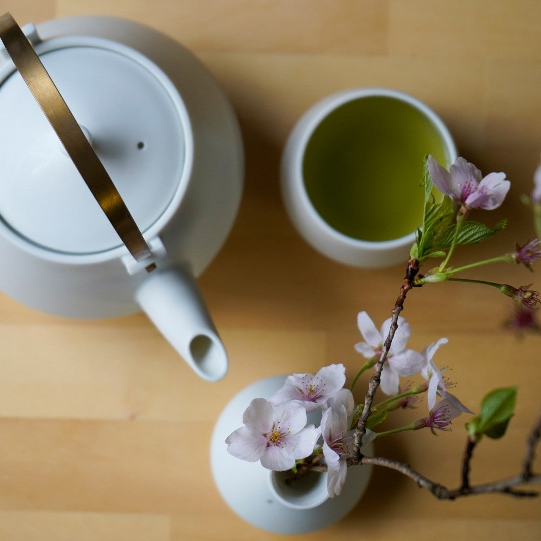 Hvid japansk tekande og yunomi tekop med grøn te ved siden af kirsebærblomster