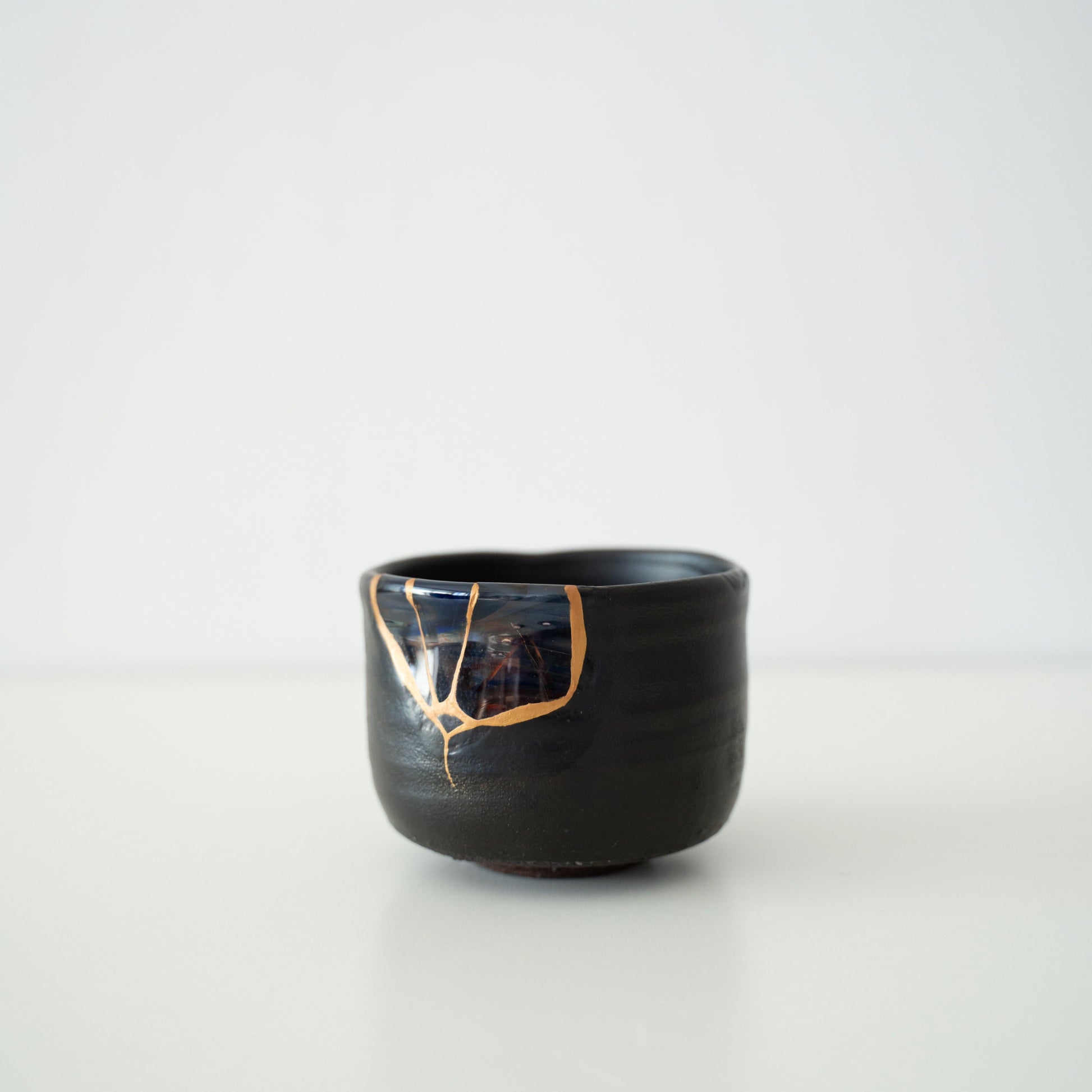 Sort Kintsugi-te skål repareret med blæst glas ved hjælp af Yobitsugi-teknikken, den mest udfordrende af Kintsugi-teknikkerne.