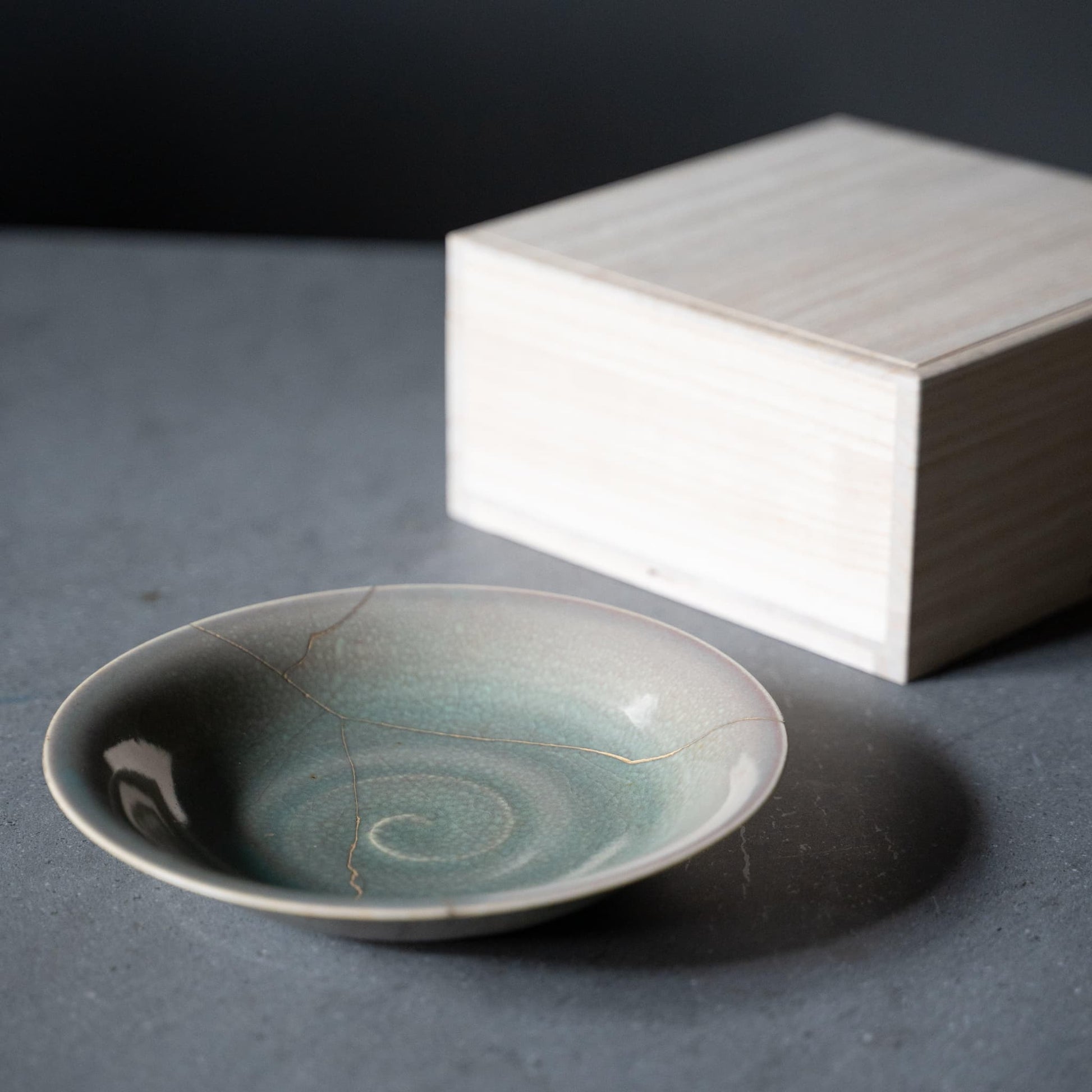 Bleggrøn skål repareret med Kintsugi, en traditionel japansk teknik, præsenteret i en paulownia-trækasse.