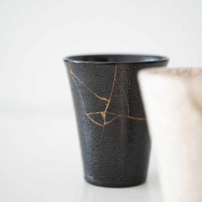 To japanske Kintsugi-kopper, én sort og én hvid, repareret med guldlak ved hjælp af den traditionelle Kintsugi-teknik.