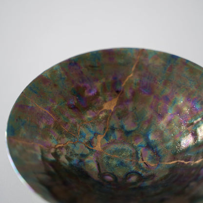 Gros plan d'une coupe de saké vert profond réparée avec du Kintsugi, une technique japonaise traditionnelle, mettant en valeur la belle jointure dorée.