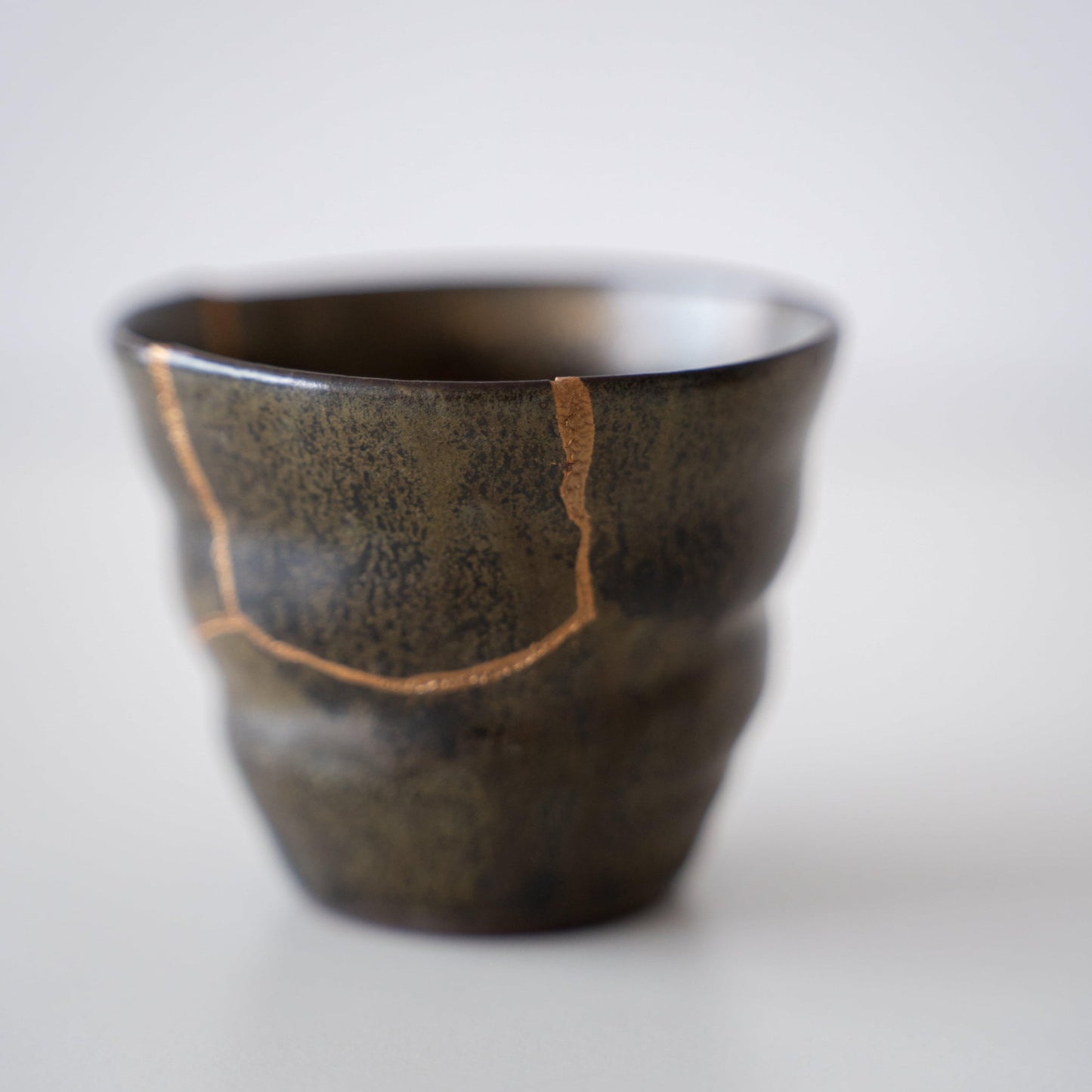 Close-up van een diepgroene sake-beker, gerepareerd met Kintsugi, een traditionele Japanse techniek, met de prachtige gouden voeg.