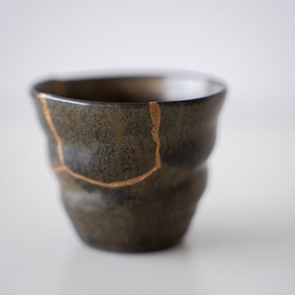 Close-up van een diepgroene sake-beker, gerepareerd met Kintsugi, een traditionele Japanse techniek, met de prachtige gouden voeg.