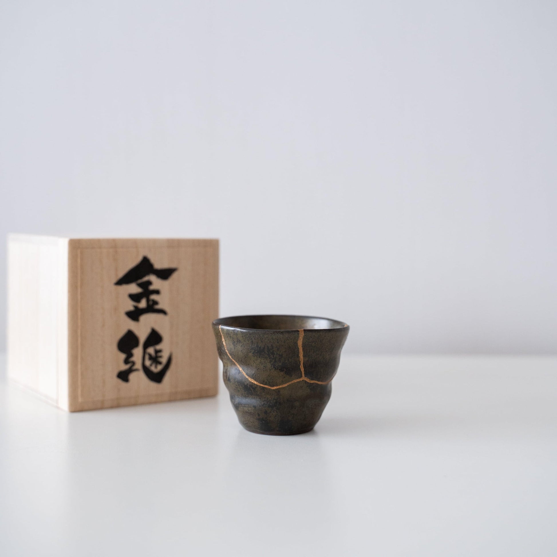 Cadeauset van een diepgroene sakebeker, gerepareerd met Kintsugi, een traditionele Japanse techniek, en een doos van paulowniahout.