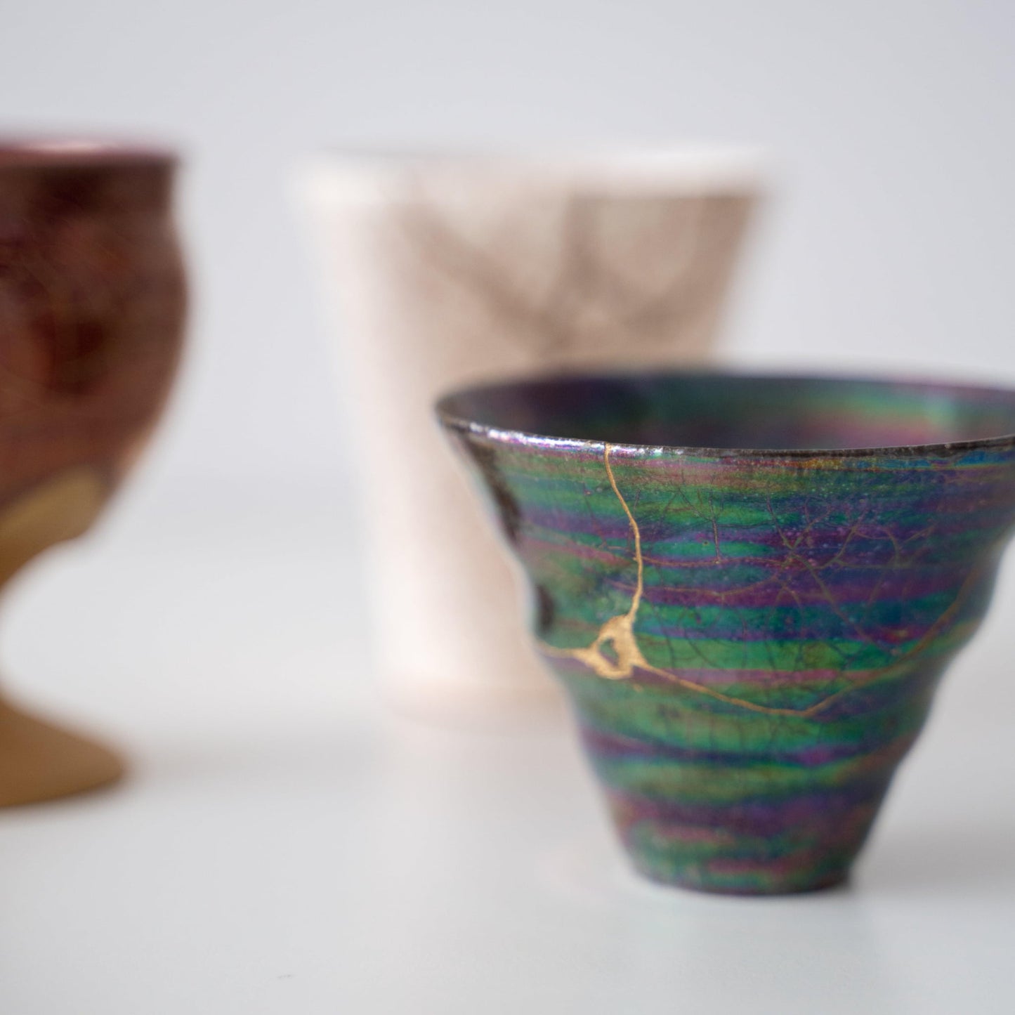 Nærbillede af en iriserende, koralformet kop repareret med Kintsugi, en traditionel japansk teknik, der viser det smukke gyldne samlingsarbejde.