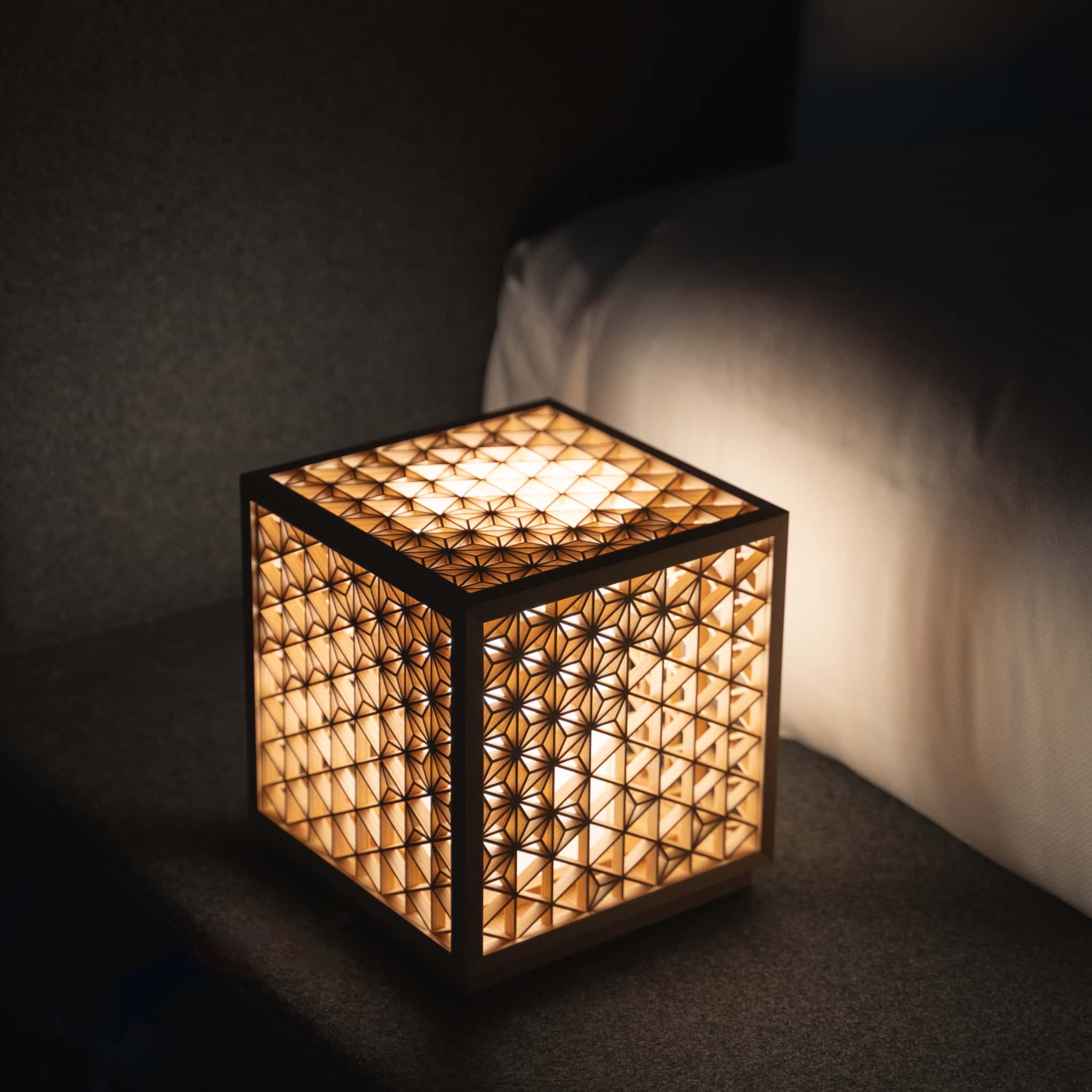 "Une lanterne Kumiko aux motifs traditionnels japonais diffuse une lumière chaude à côté d'un lit dans une chambre faiblement éclairée"